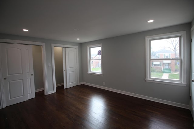 unfurnished bedroom with dark wood-style flooring, multiple closets, and multiple windows
