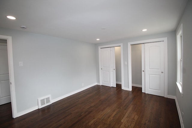 unfurnished bedroom with recessed lighting, two closets, dark wood-type flooring, and visible vents