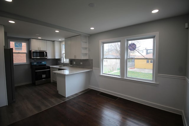kitchen with open shelves, a sink, a peninsula, stainless steel microwave, and electric stove