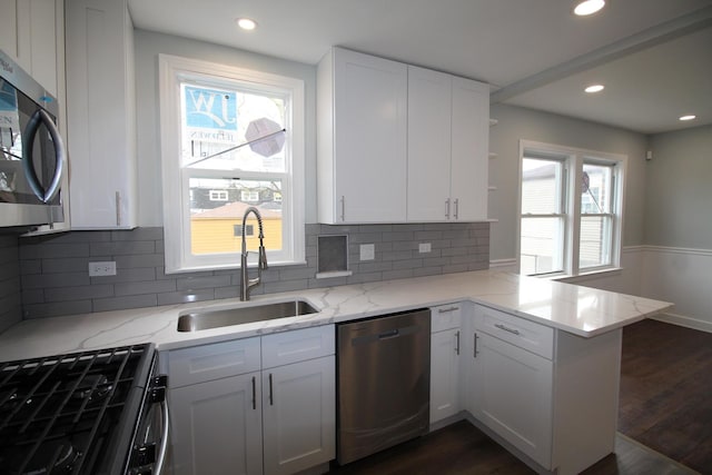 kitchen with a sink, white cabinetry, a peninsula, and stainless steel appliances