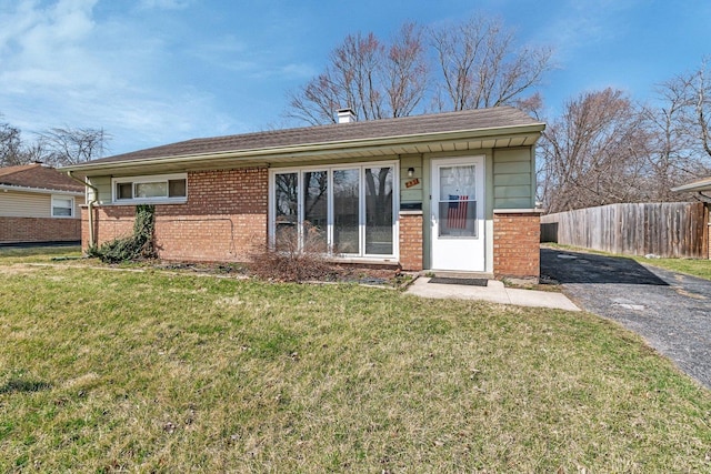 ranch-style home featuring brick siding, a front lawn, fence, and driveway