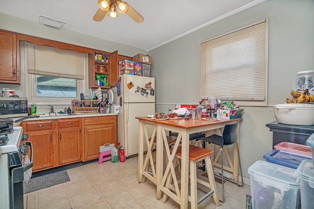 kitchen with a ceiling fan, gas range, crown molding, light tile patterned floors, and freestanding refrigerator