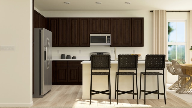 kitchen with dark brown cabinetry, a kitchen bar, light wood-type flooring, light countertops, and stainless steel appliances