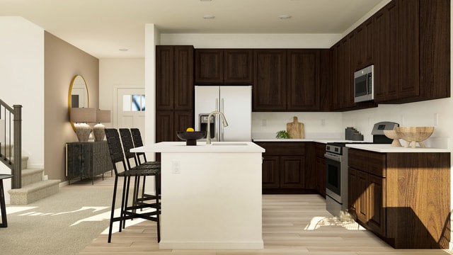 kitchen with appliances with stainless steel finishes, light wood-type flooring, dark brown cabinets, a sink, and light countertops
