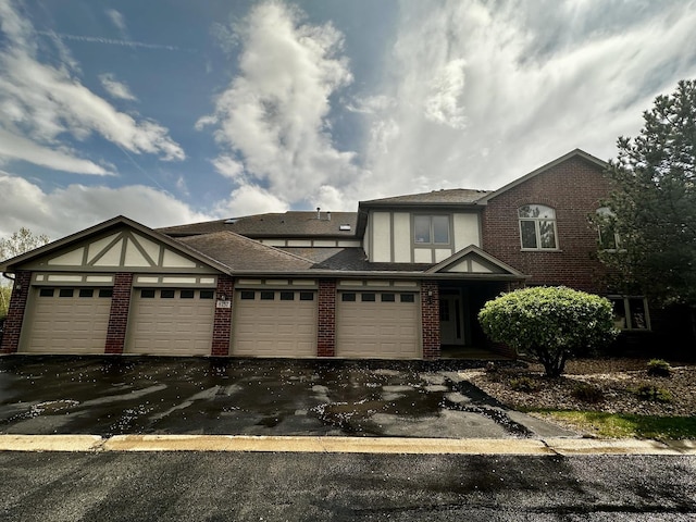 view of front of property featuring brick siding, an attached garage, a shingled roof, and aphalt driveway