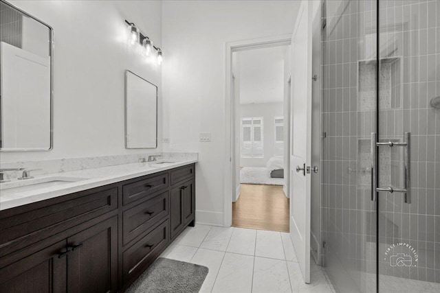 ensuite bathroom featuring a tile shower, double vanity, and baseboards