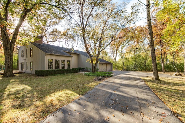 view of side of property featuring a garage, aphalt driveway, a yard, and a chimney