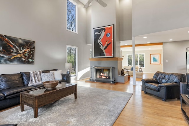 living area with a glass covered fireplace, a towering ceiling, ceiling fan, recessed lighting, and light wood-style flooring