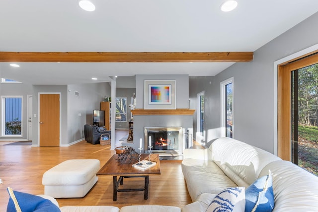 living area featuring visible vents, beam ceiling, wood finished floors, a glass covered fireplace, and recessed lighting
