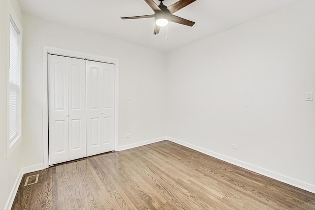 unfurnished bedroom with visible vents, a closet, wood finished floors, baseboards, and ceiling fan