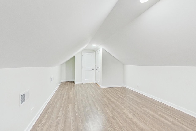additional living space with baseboards, vaulted ceiling, light wood-style flooring, and visible vents