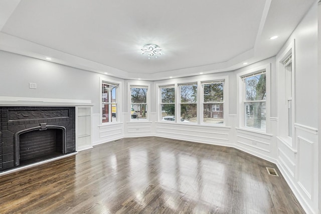 unfurnished living room featuring visible vents, a decorative wall, a fireplace, and wood finished floors