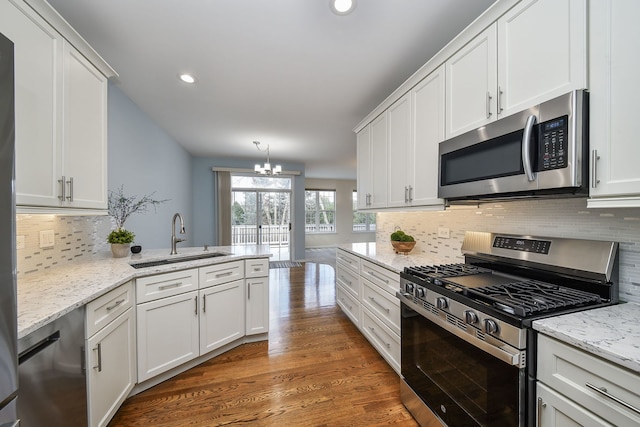 kitchen with decorative backsplash, white cabinets, a sink, appliances with stainless steel finishes, and a notable chandelier