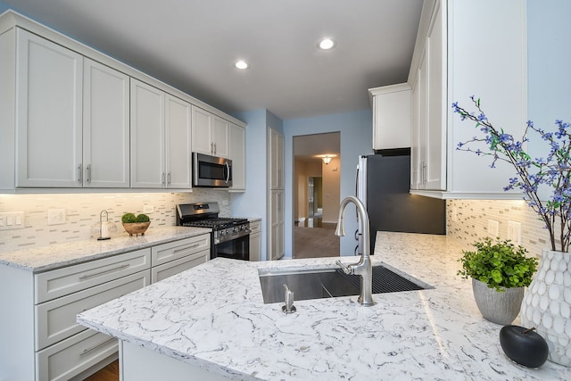 kitchen featuring light stone counters, a sink, decorative backsplash, and appliances with stainless steel finishes