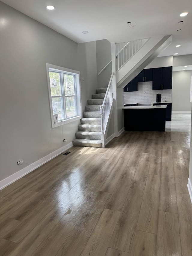 unfurnished living room with stairway, baseboards, recessed lighting, and light wood-style flooring