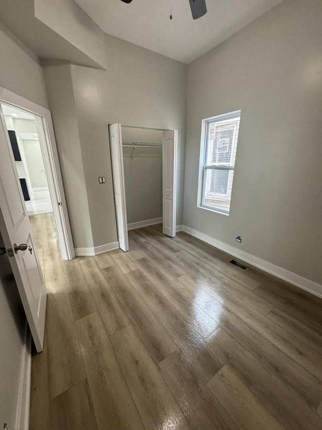 unfurnished bedroom featuring ceiling fan, visible vents, baseboards, a closet, and light wood-style floors