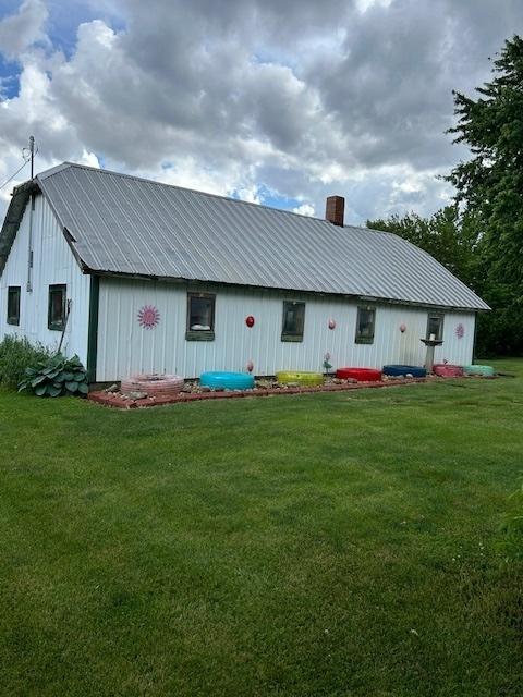rear view of house with an outbuilding, a chimney, a yard, and metal roof