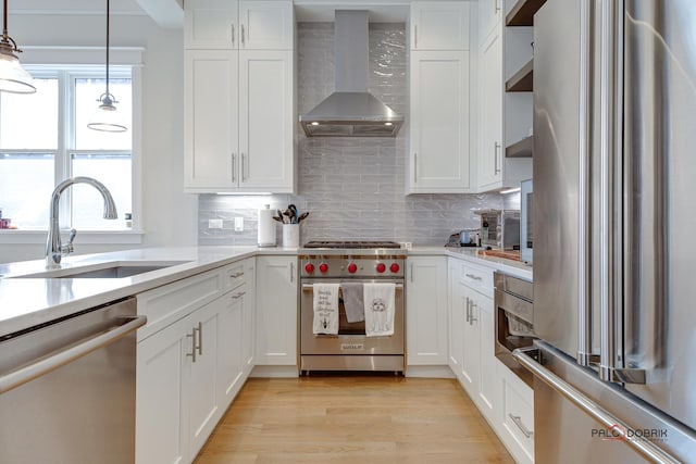 kitchen featuring wall chimney range hood, a sink, light countertops, stainless steel appliances, and white cabinetry