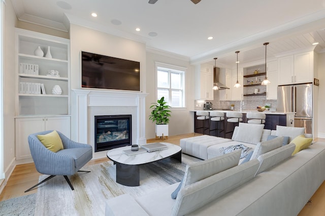 living room featuring crown molding, a glass covered fireplace, recessed lighting, a ceiling fan, and light wood finished floors