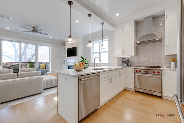 kitchen with wall chimney range hood, appliances with stainless steel finishes, a sink, white cabinets, and open floor plan