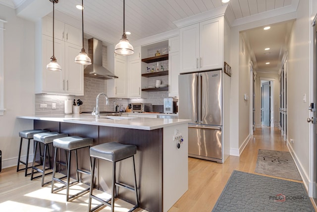 kitchen with open shelves, a breakfast bar, high end fridge, wall chimney exhaust hood, and light wood finished floors