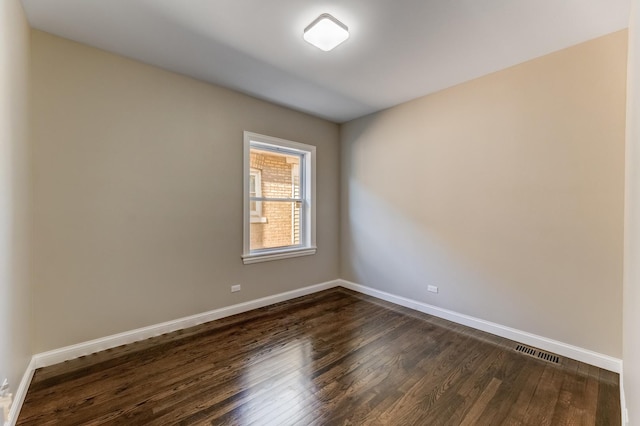empty room featuring visible vents, dark wood-style flooring, and baseboards