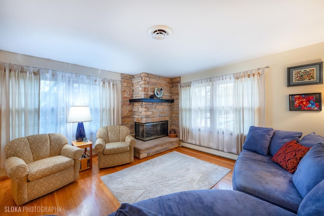living area featuring a fireplace, plenty of natural light, wood finished floors, and a baseboard radiator