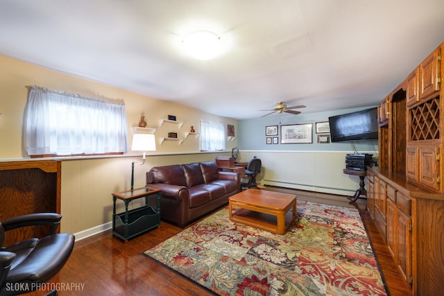 living room featuring dark wood-type flooring, ceiling fan, a baseboard heating unit, and a wainscoted wall