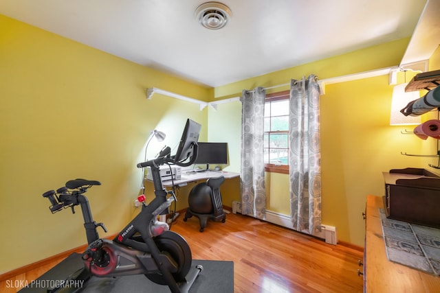 workout area with baseboards, a baseboard radiator, wood finished floors, and visible vents