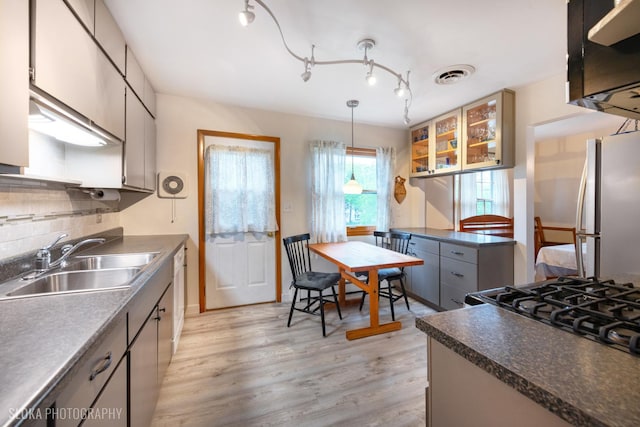 kitchen with dark countertops, a sink, freestanding refrigerator, light wood-type flooring, and tasteful backsplash