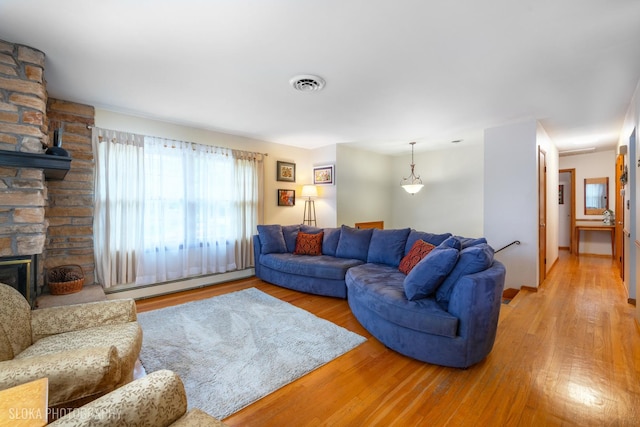 living room with a fireplace, a baseboard heating unit, wood finished floors, and visible vents