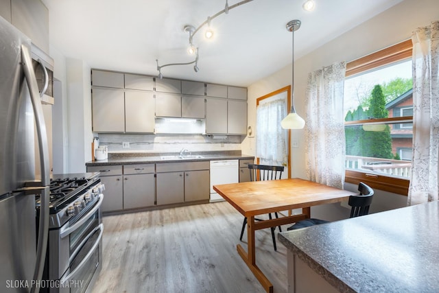 kitchen with decorative backsplash, dark countertops, light wood-type flooring, a sink, and stainless steel appliances