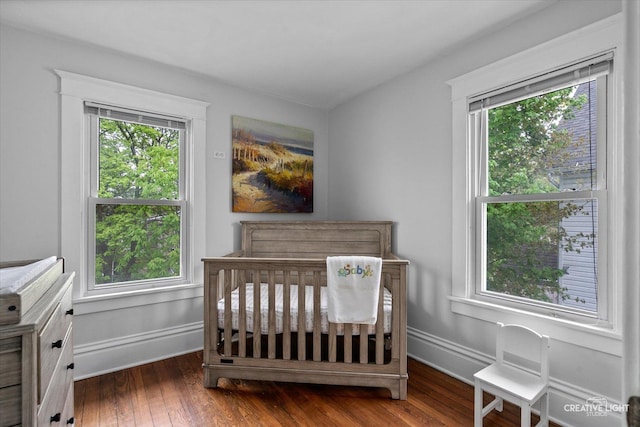 bedroom with a nursery area, baseboards, multiple windows, and hardwood / wood-style flooring