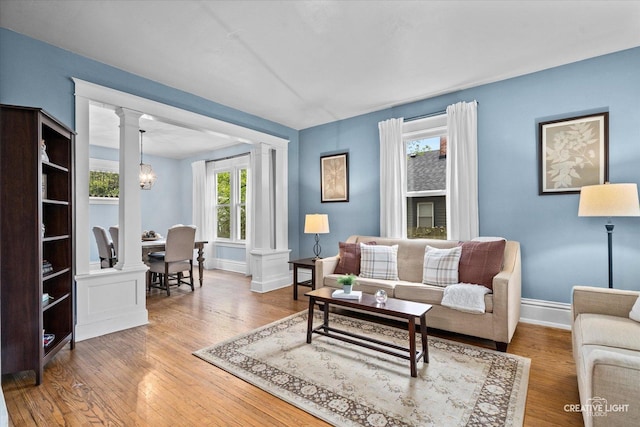 living room featuring a chandelier, baseboards, decorative columns, and wood finished floors