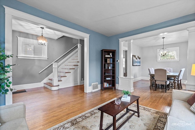 living area featuring a notable chandelier, wood finished floors, ornate columns, visible vents, and stairway