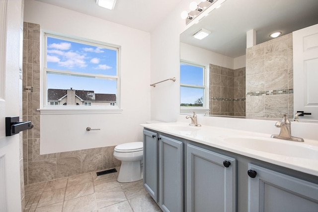 full bath featuring double vanity, a sink, visible vents, and toilet