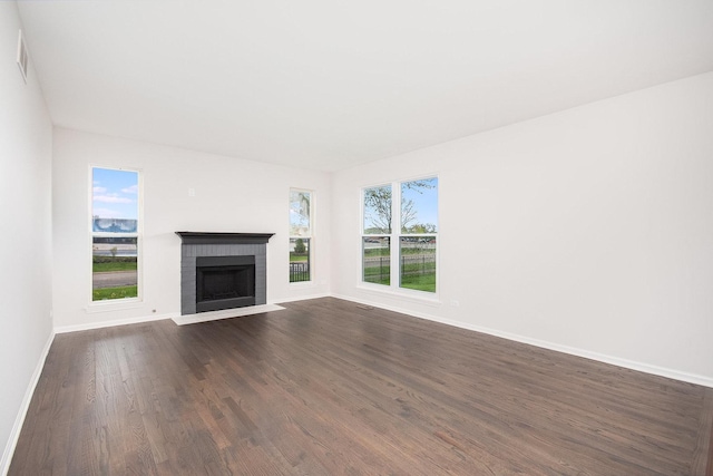 unfurnished living room with visible vents, dark wood finished floors, a brick fireplace, and baseboards