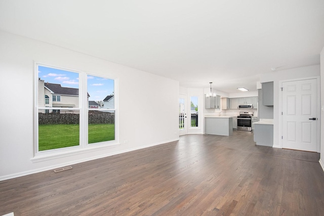 unfurnished living room with baseboards, dark wood-style flooring, a chandelier, and visible vents