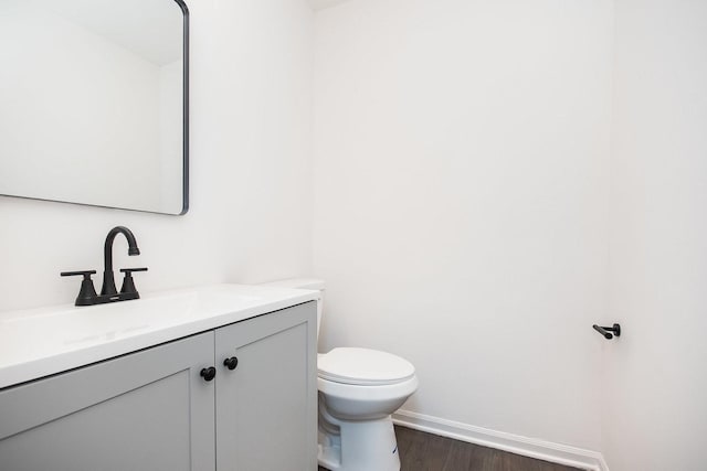 half bathroom with vanity, baseboards, toilet, and wood finished floors