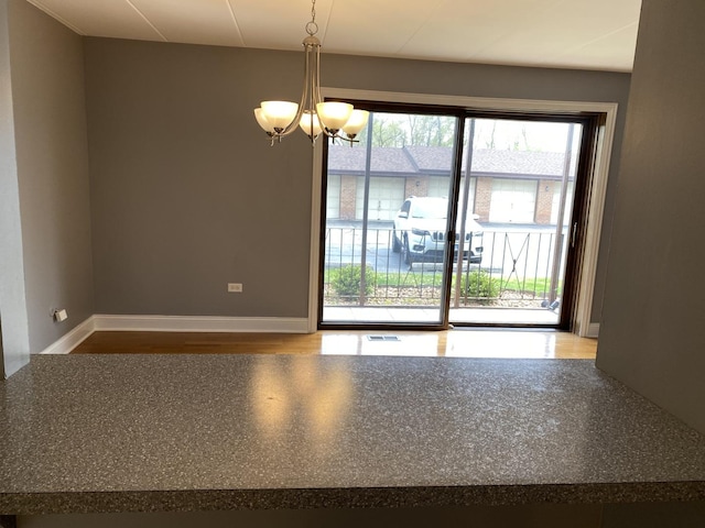 unfurnished room featuring visible vents, baseboards, wood finished floors, and a notable chandelier