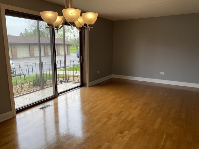 unfurnished room with visible vents, baseboards, wood finished floors, and a notable chandelier