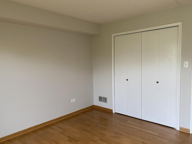 unfurnished bedroom featuring visible vents, baseboards, wood finished floors, and a closet