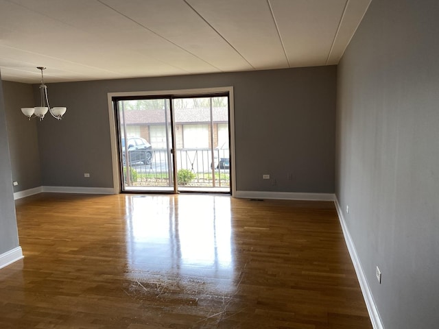 spare room featuring baseboards, wood finished floors, and a chandelier
