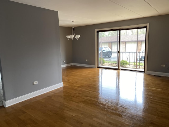 empty room with baseboards, a notable chandelier, and dark wood-style floors