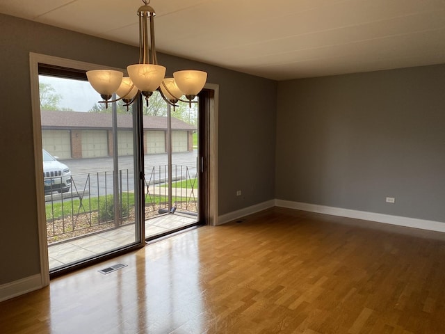 spare room with visible vents, a notable chandelier, wood finished floors, and a wealth of natural light
