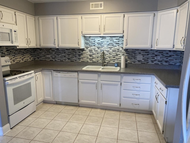 kitchen featuring dark countertops, a sink, white appliances, backsplash, and visible vents