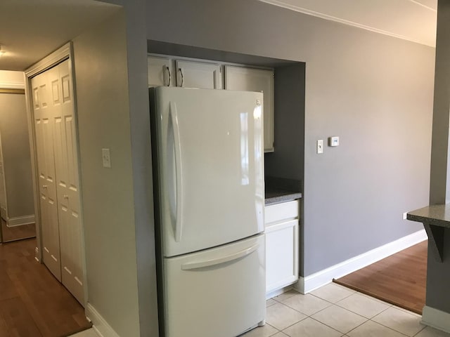 kitchen with baseboards, freestanding refrigerator, light tile patterned floors, and white cabinets