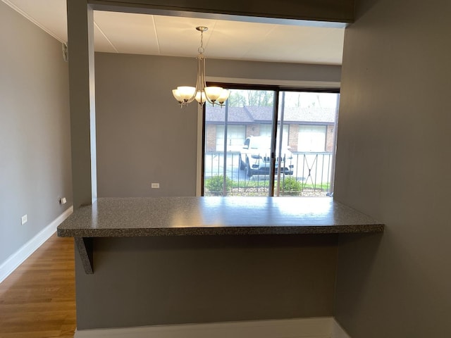 kitchen featuring dark countertops, a notable chandelier, decorative light fixtures, baseboards, and wood finished floors
