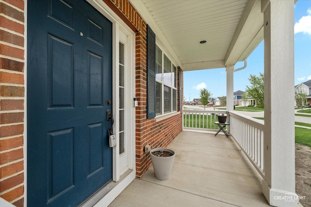 view of exterior entry featuring covered porch, brick siding, and a residential view