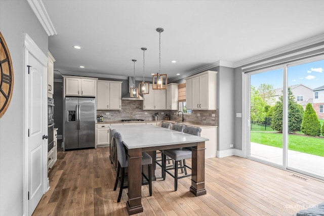 kitchen featuring ornamental molding, a kitchen breakfast bar, light countertops, wall chimney exhaust hood, and appliances with stainless steel finishes